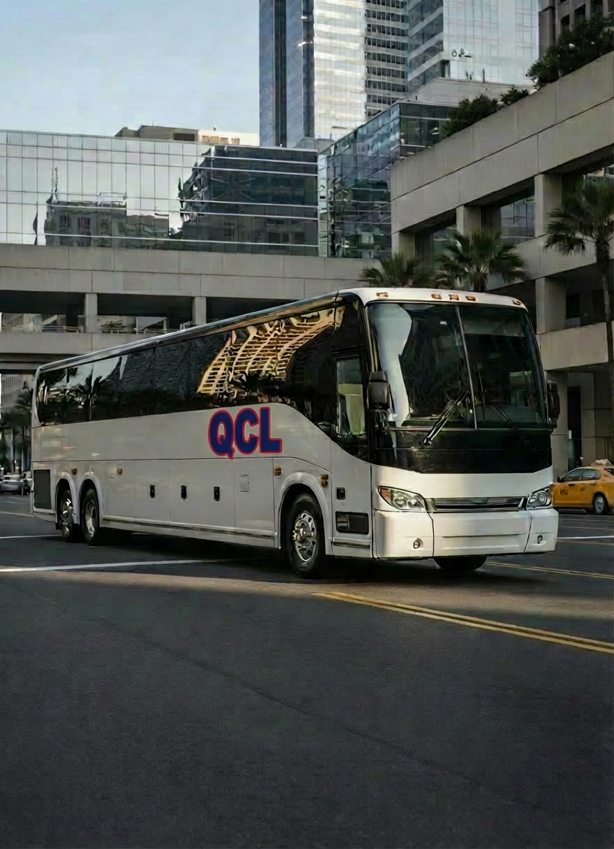 A modern luxury charter bus with a sleek white exterior, subtle silver accents, and tinted panoramic windows is parked in front of a contemporary city convention center. The polished bodywork reflects the clean lines of glass and steel buildings around it. Early morning natural light creates soft highlights along the bus’s contours and casts crisp shadows on the smooth asphalt. The scene is composed at eye level with the bus angled three-quarters toward the viewer, giving a clear view of its length and professional branding area. The background is slightly blurred for emphasis, and the overall photographic realism feels clean, professional, and reliable, perfect for representing premium charter bus service.